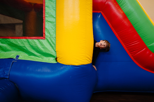 Child playing on a colorful inflatable bounce house with blue, yellow, red, and green vinyl panels.