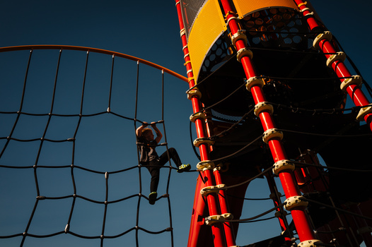 Person climbing a red and yellow climbing wall structure against a clear blue sky.
