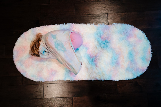 Overhead view of a child wrapped in a fluffy pastel-colored blanket on a wooden floor.