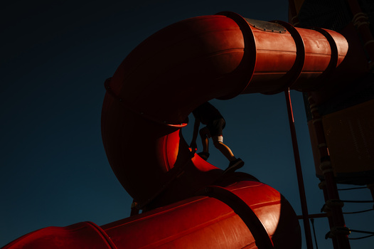 Red industrial pipe and valve structure silhouetted against a deep blue twilight sky.