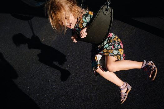 Child on tire swing suspended from above, photographed from directly overhead against dark ground.
