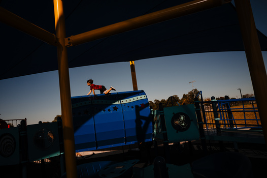 Person sitting on blue industrial truck cab at dusk, framed by wooden pergola structure.