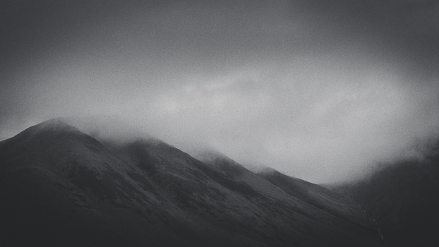Misty mountain peaks emerging from dense fog under an overcast sky.