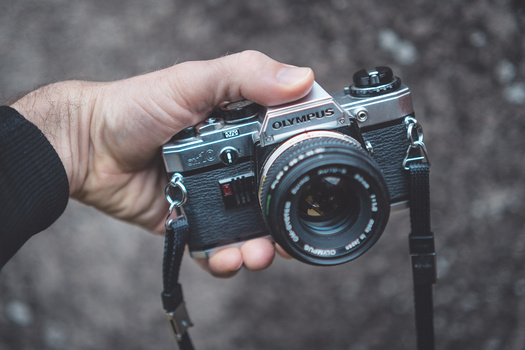 Hand holding a vintage Olympus film camera with a dark textured background.