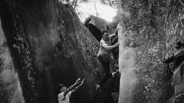 Two climbers navigating a narrow rock crevasse in black and white photography.
