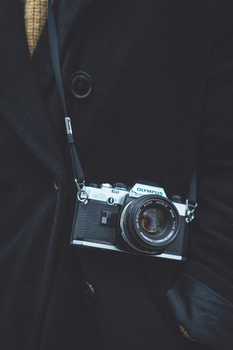 Vintage rangefinder camera with leather neck strap hanging against dark clothing.