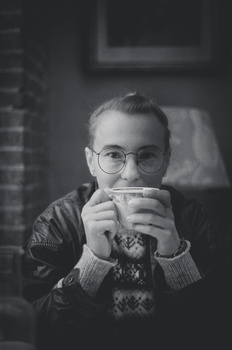 Person wearing glasses and a sweater holds a mug up to their face in black and white portrait.