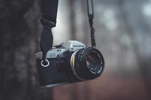 Olympus film camera with 50mm lens suspended by a black strap against a blurred background.