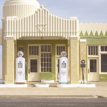 Illustration of a vintage gas station with cream-colored brick facade and green Art Deco roof details.