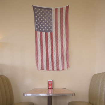 American flag tapestry hanging on a neutral wall above a small table with two chairs.