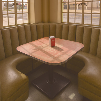 Minimalist booth interior with pink-topped table, olive banquette seating, and gridded windows casting geometric shadows.