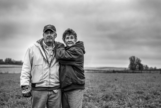 Two people standing together in an open field under an overcast sky.