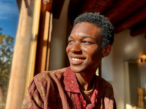 Person smiling outdoors in warm golden-hour sunlight, wearing a burgundy patterned shirt.