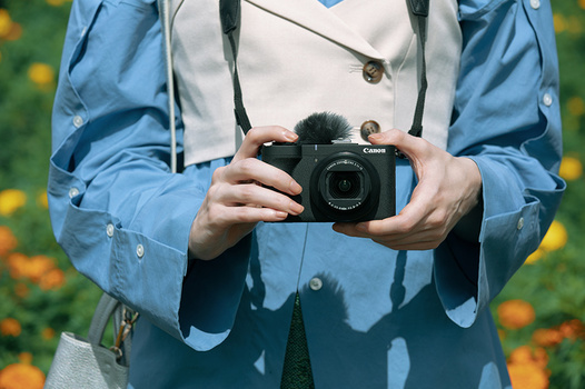 Photographer holding a vintage rangefinder camera with a fur pom-pom accessory, wearing a blue jacket.