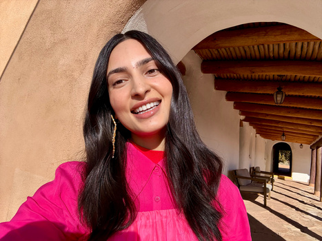 Woman in bright pink shirt smiling at camera in covered colonial-style walkway.
