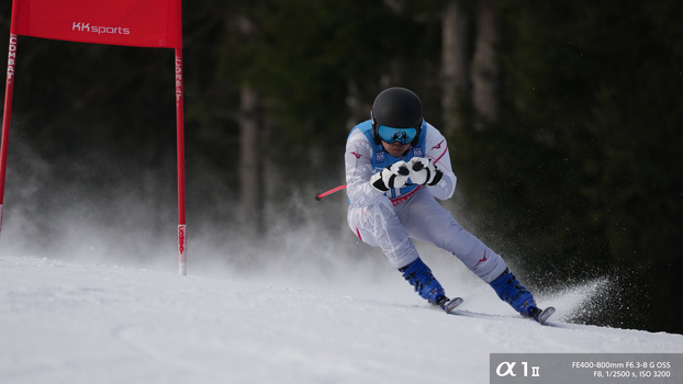 Alpine skier navigating a slalom gate during competition with heavy snow spray.