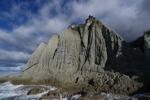 Dramatic columnar basalt rock formation rising from ocean waves under cloudy sky.