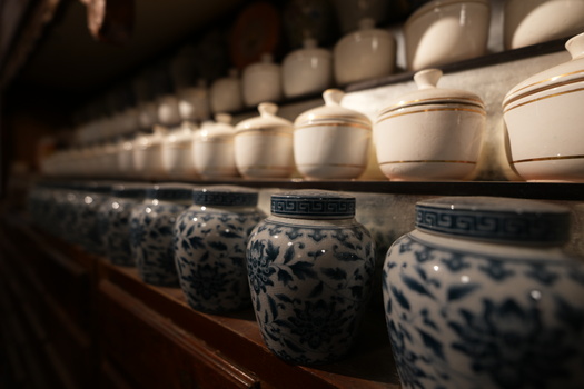 Blue and white ceramic vessels with decorative patterns arranged in rows on wooden shelving, with shallow depth of field.