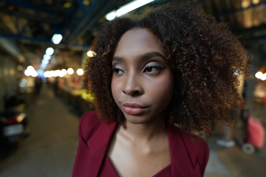 Woman with natural curly hair wearing burgundy blazer in urban nighttime setting.