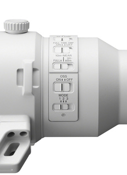 Close-up view of a white camera lens showing manual focus ring, zoom controls, and mode buttons on the barrel.
