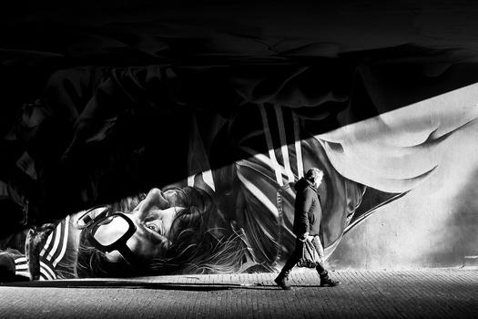 Silhouetted figure standing beneath draped fabric with dramatic overhead lighting casting strong shadows.