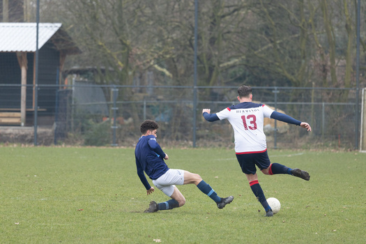Youth soccer player in white jersey number 13 challenges opponent in blue during match on grass field.