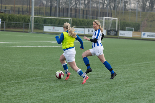 Young female soccer player in yellow and blue jersey dribbling ball while opponent in blue and white stripes defends.