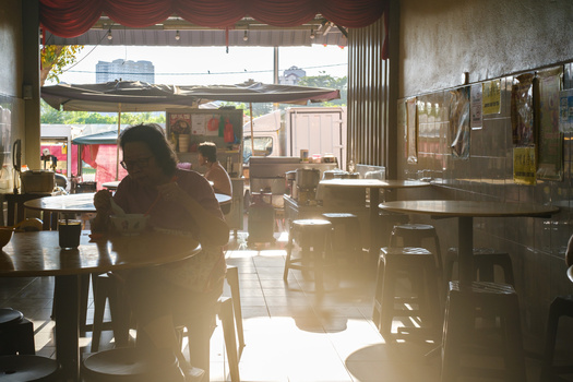 Silhouetted person sitting at a table in a bright, sunlit interior space with industrial architecture.