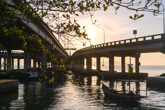 Concrete bridge overpass spanning calm water with a moored boat beneath, shot at golden hour.