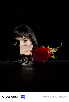 Woman's face in profile against black background with red rose positioned at her mouth.