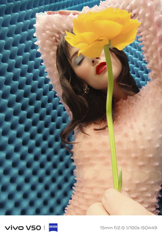 Woman holding yellow flower against textured blue and pink foam backdrop.