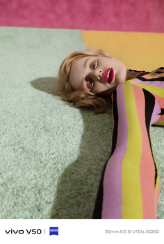 Person lying on mint green carpet wearing colorful striped clothing against pastel background.