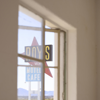 Neon vintage motel sign reflected in window glass with desert landscape beyond.