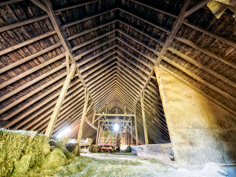 Interior of a timber-framed barn at night, showing exposed wooden beams converging toward a central vanishing point.