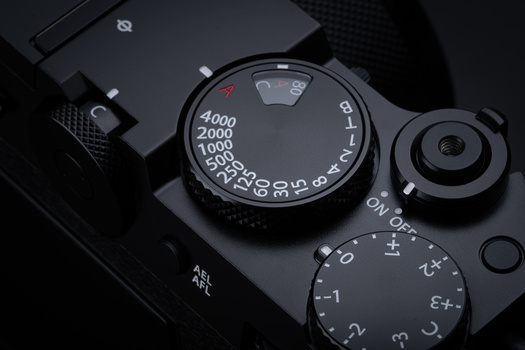 Close-up of camera exposure compensation dial and shutter speed dial on black camera body.