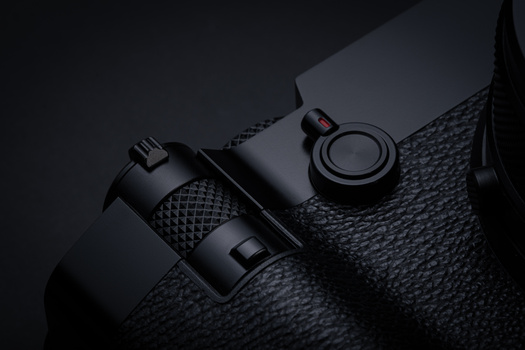 Two black camera lenses with textured grip surfaces arranged on a dark fabric background.