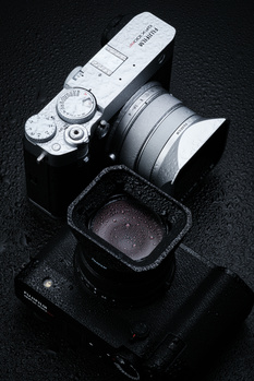 Overhead view of a mirrorless camera with attached lens and accessories on dark textured surface.