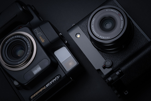 Three compact digital cameras with prime lenses arranged on a dark textured surface.