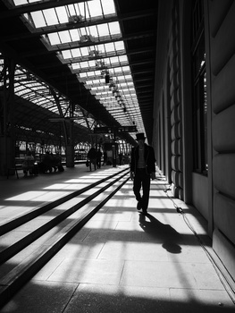 Silhouetted figure walking through a modern corridor with geometric skylights casting strong linear shadows on the floor.