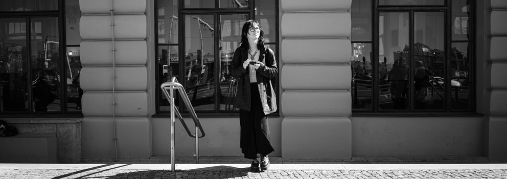 Woman in dark coat standing on paved street with storefront behind her in black and white photograph.