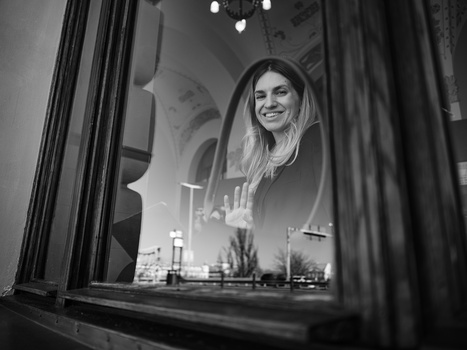 Woman smiling through window with city skyline reflection in black and white.