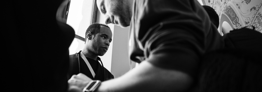 Man in dark clothing looking toward camera during what appears to be an indoor interaction or discussion.