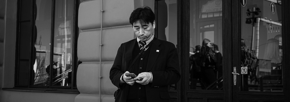 Man in dark blazer looking down at his phone while standing in a modern transit station.