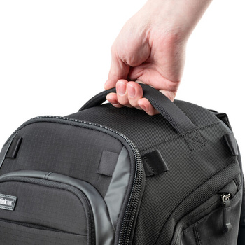 Hand gripping the carry handle of a dark gray and black camera backpack.