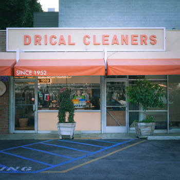 Storefront of Drical Cleaners, a dry cleaning business operating since 1952, with orange awning and blue handicap parking spaces in front.