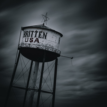 Weathered water tower with "BRITTEN USA" text against a dramatic, stormy sky.