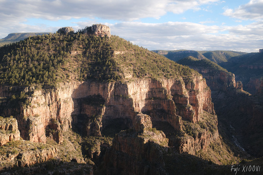 Dramatic sandstone cliff formations with layered rock faces and dense forest coverage on a mountainous landscape.