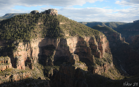 Dramatic sandstone cliffs and forested ridges under partly cloudy sky.