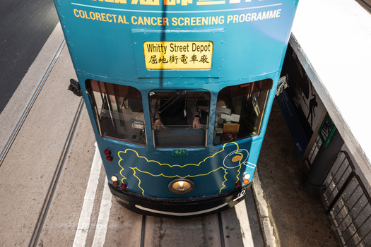 Overhead view of a blue double-decker tram with colorectal cancer screening signage, shot from directly above.
