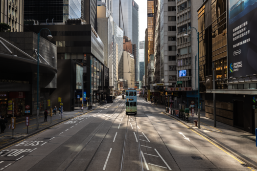 Empty urban street with tall buildings, tram tracks, and dramatic shadows from morning sunlight.